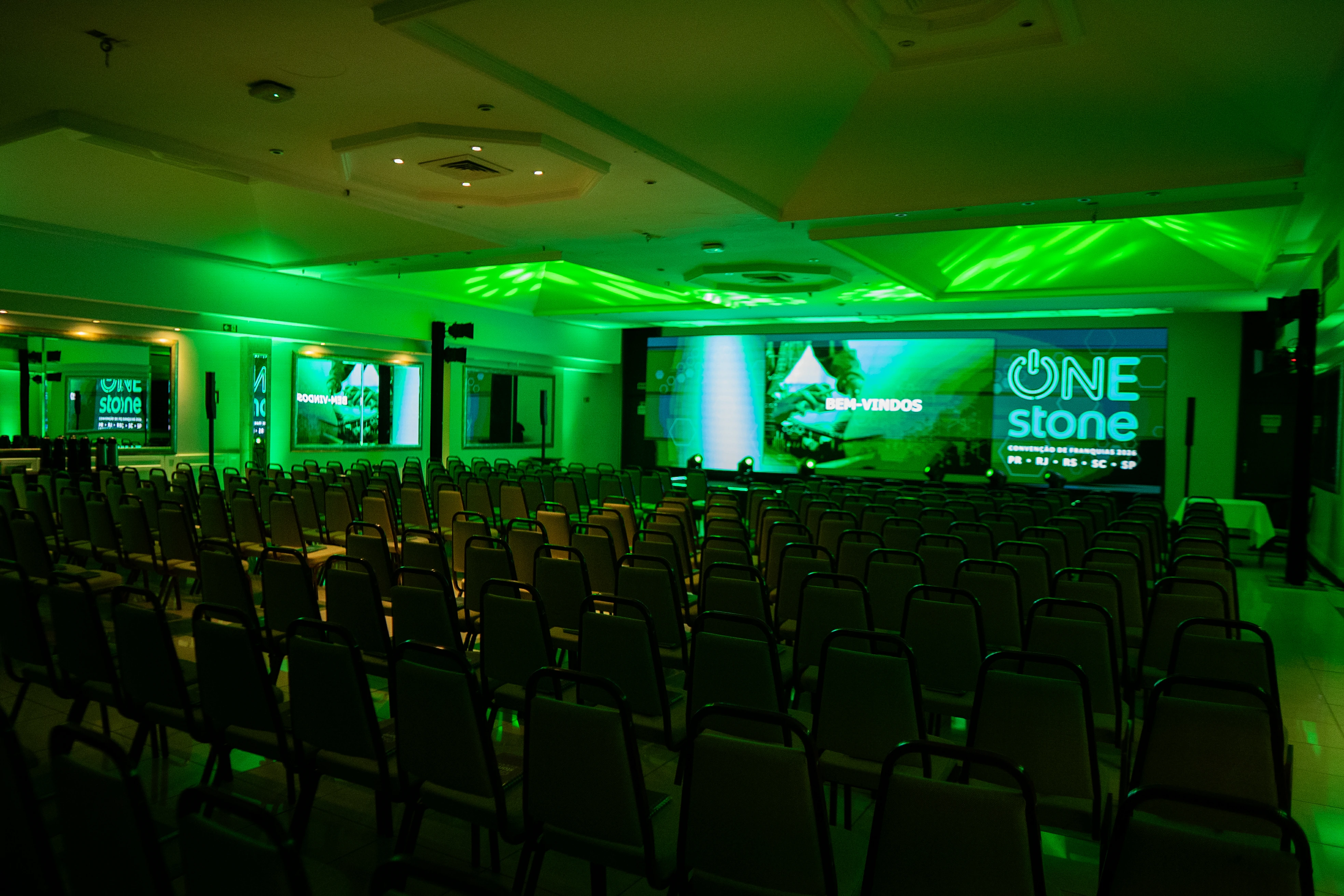 Salão do One Stone com cadeiras, palco e iluminação verde